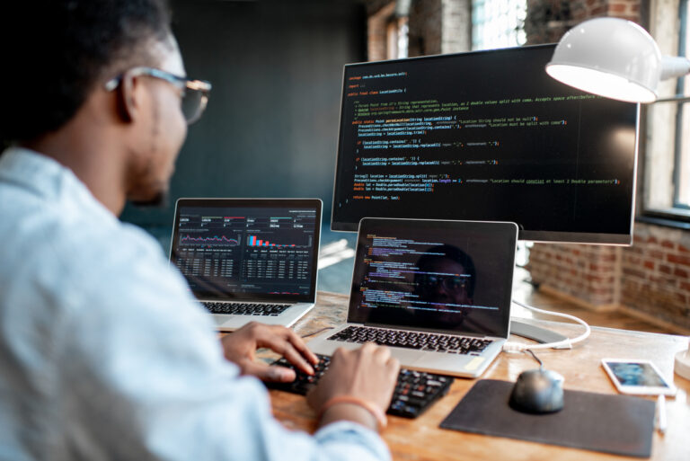 A man utilizing two laptops at a desk, unlocking marketing performance through algorithmic attribution.