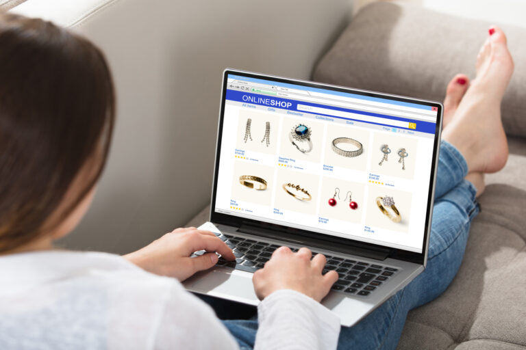 A woman is sitting on a couch browsing jewelry on her laptop while referring to a guide for conversion optimization.