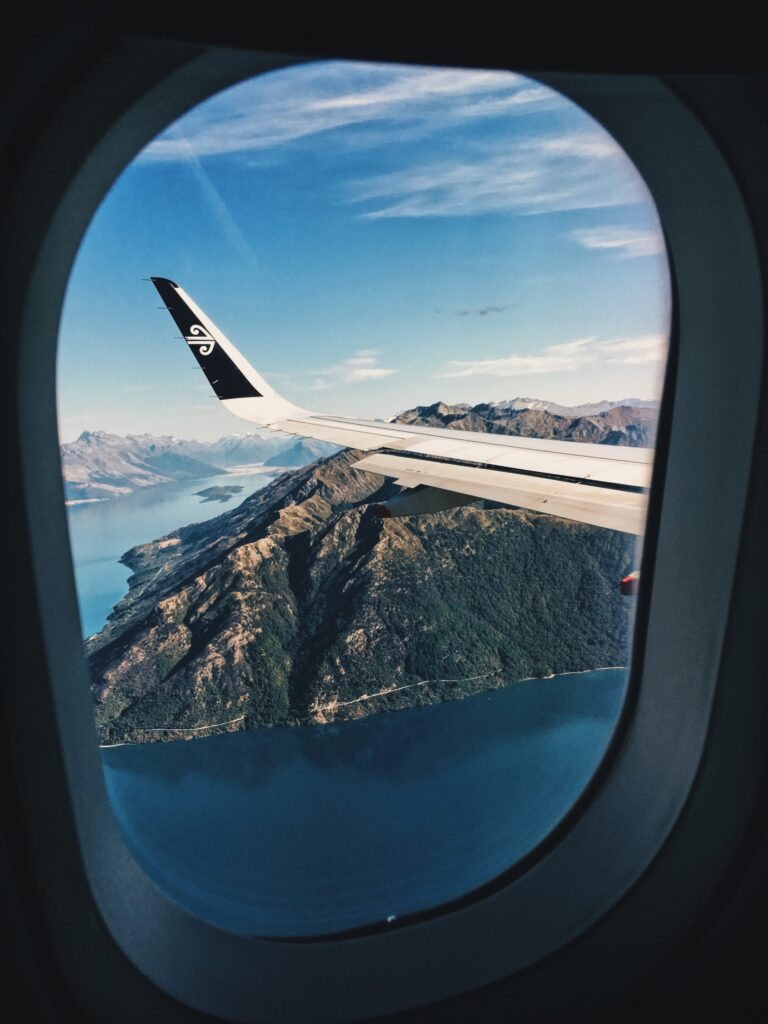 An airplane window with a view of a lake and mountains in the tourism and travel industries.